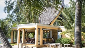 Una casa moderna frente al mar con un porche cubierto, mobiliario exterior y vistas al océano.