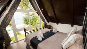 Un dormitorio con un ventanal grande, una cama con toallas y vistas a la playa.
