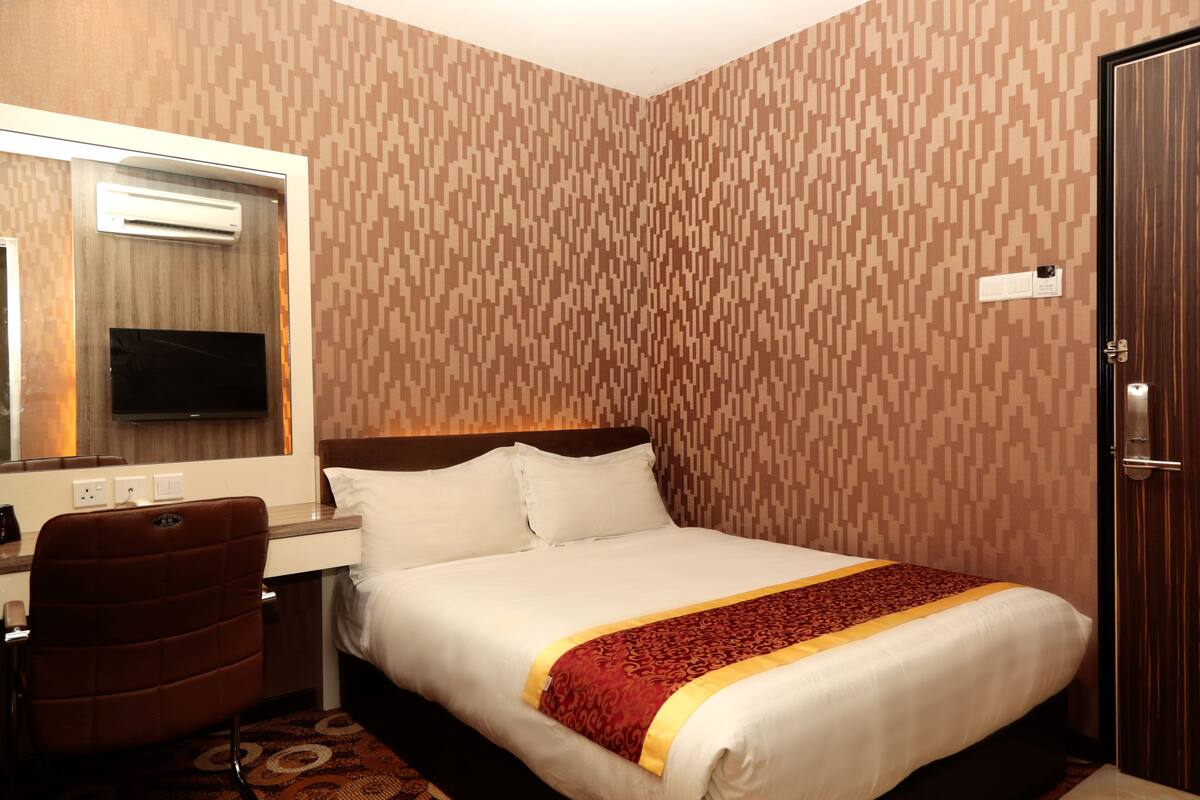 Una habitación de hotel con cama, escritorio, silla, espejo y puerta.