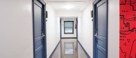 Un pasillo con puertas azules, un extintor y una pared roja con un diseño que recuerda a un circuito.