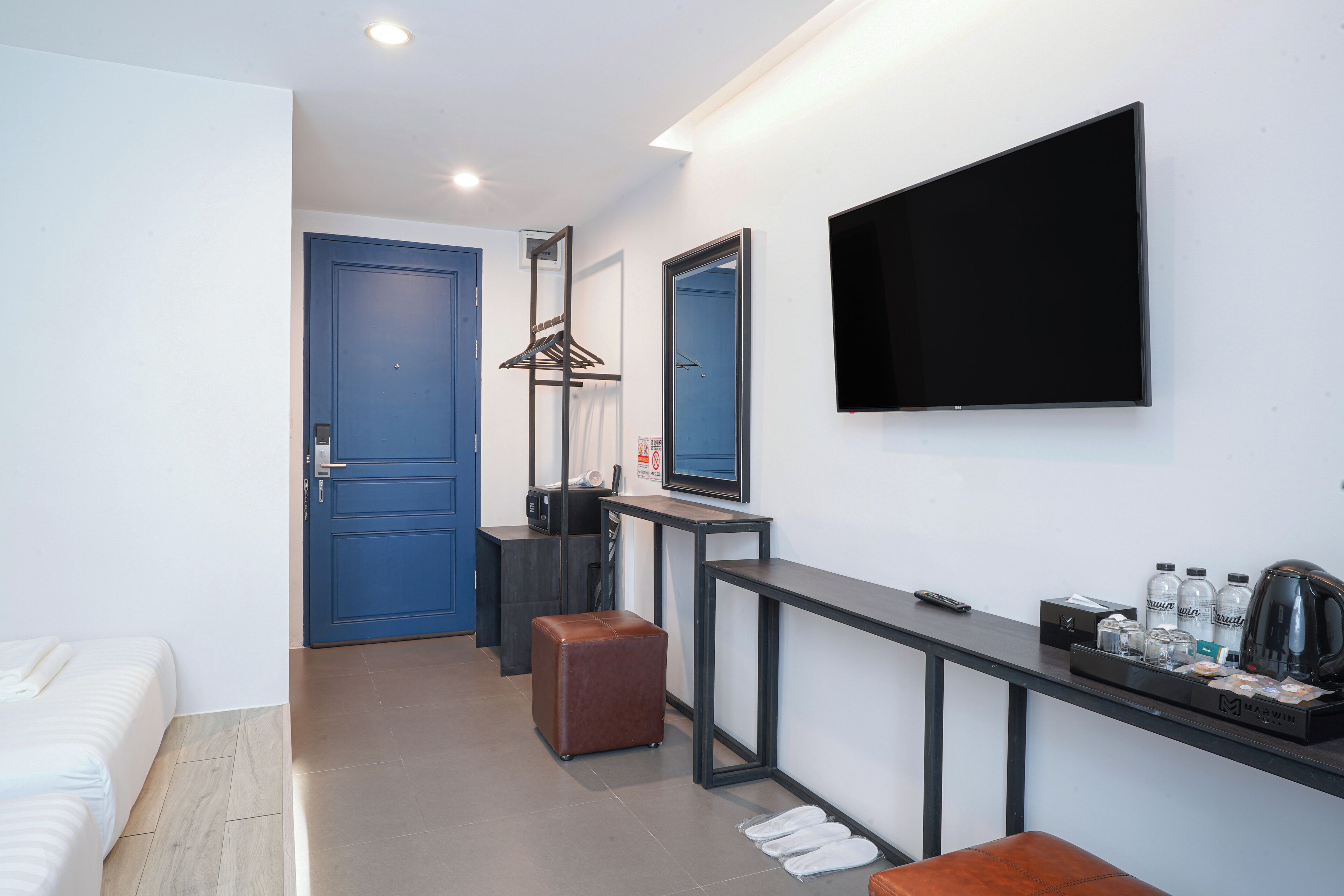 A modern hotel room with a bed, a desk with a flat-screen TV, a coffee maker, and a minibar.