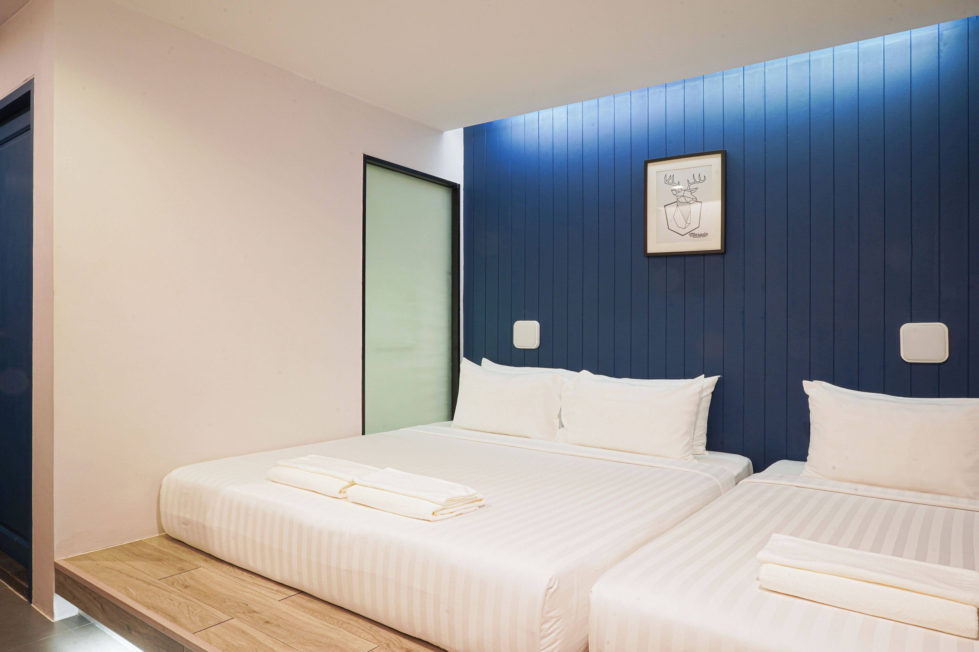 A hotel room with two beds, a wooden floor, a blue accent wall, and a framed artwork.