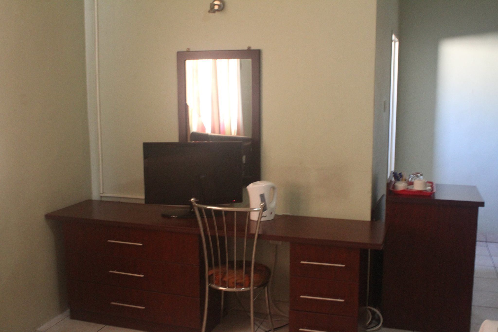 Un escritorio pequeño de madera oscura con una silla, un espejo y un televisor.