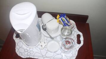 A tray with a coffee maker, cups, a glass, and some packets on a table.