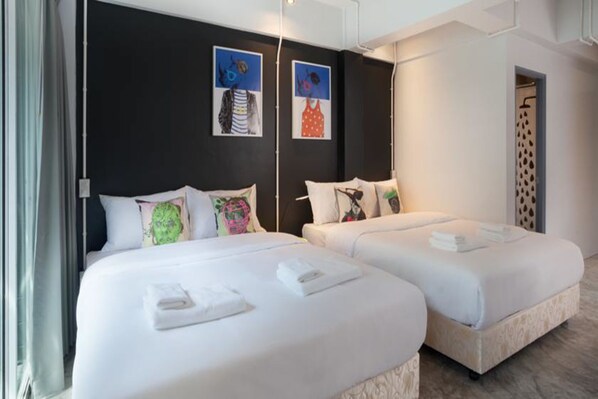 A hotel room with two beds, a dark wall with artwork, a shower area, and a window with curtains.