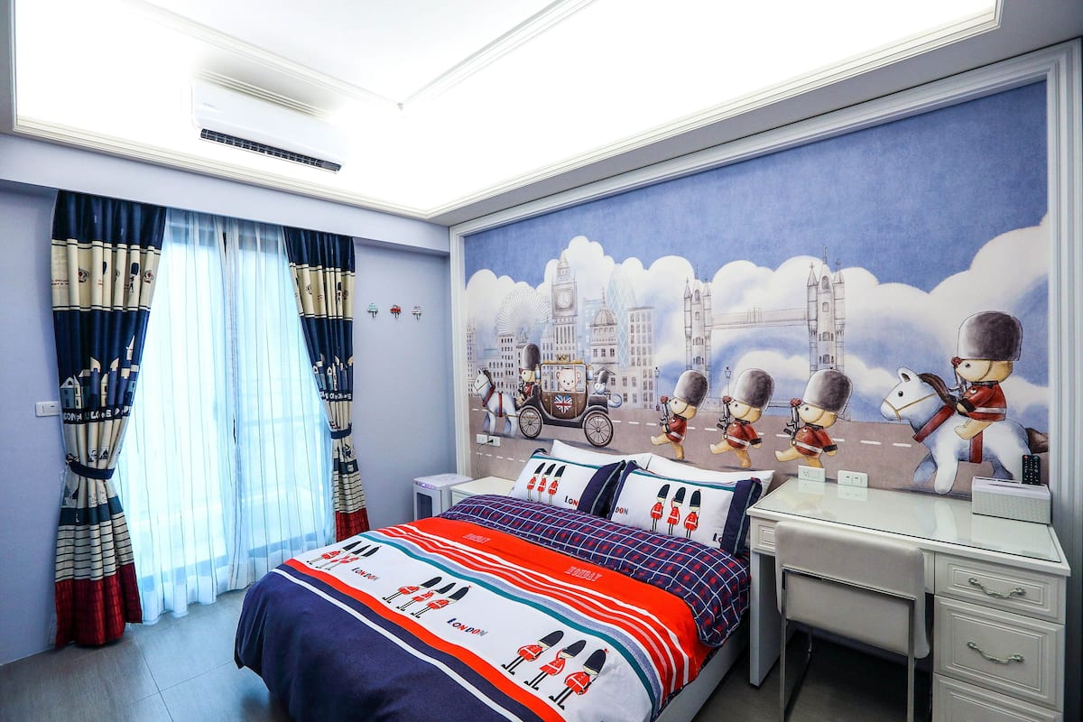 A hotel room with a bed, a desk, and a mural of London landmarks.
