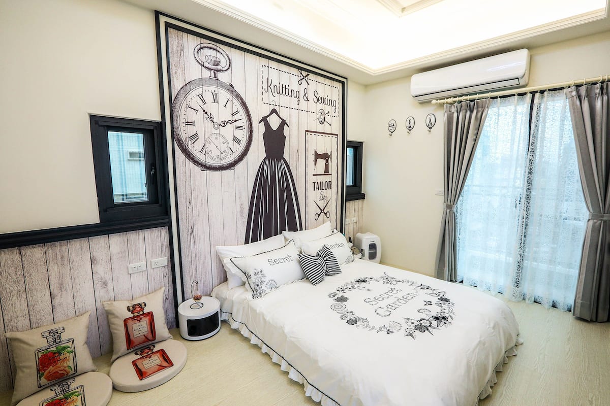 A bedroom with a bed, a wall clock, and a window with curtains.