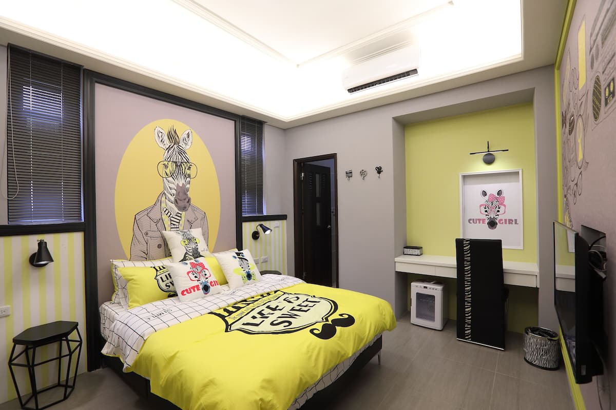 A bedroom with a bed, a small table, a mirror, a TV, and a door.