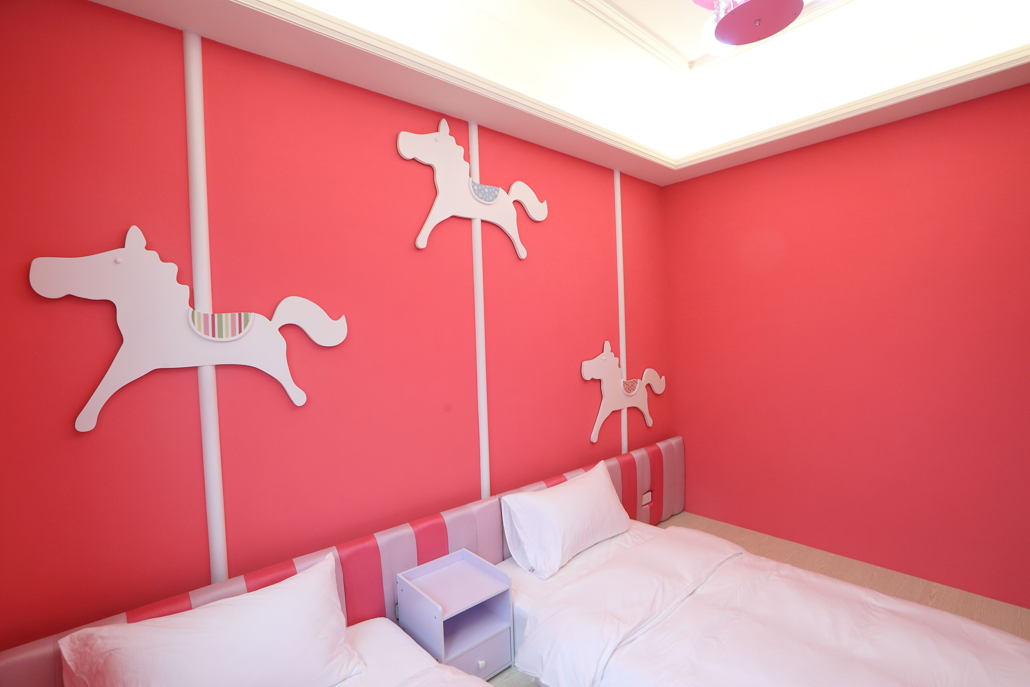 A bedroom with a red wall, white bed, and three white horse decorations.