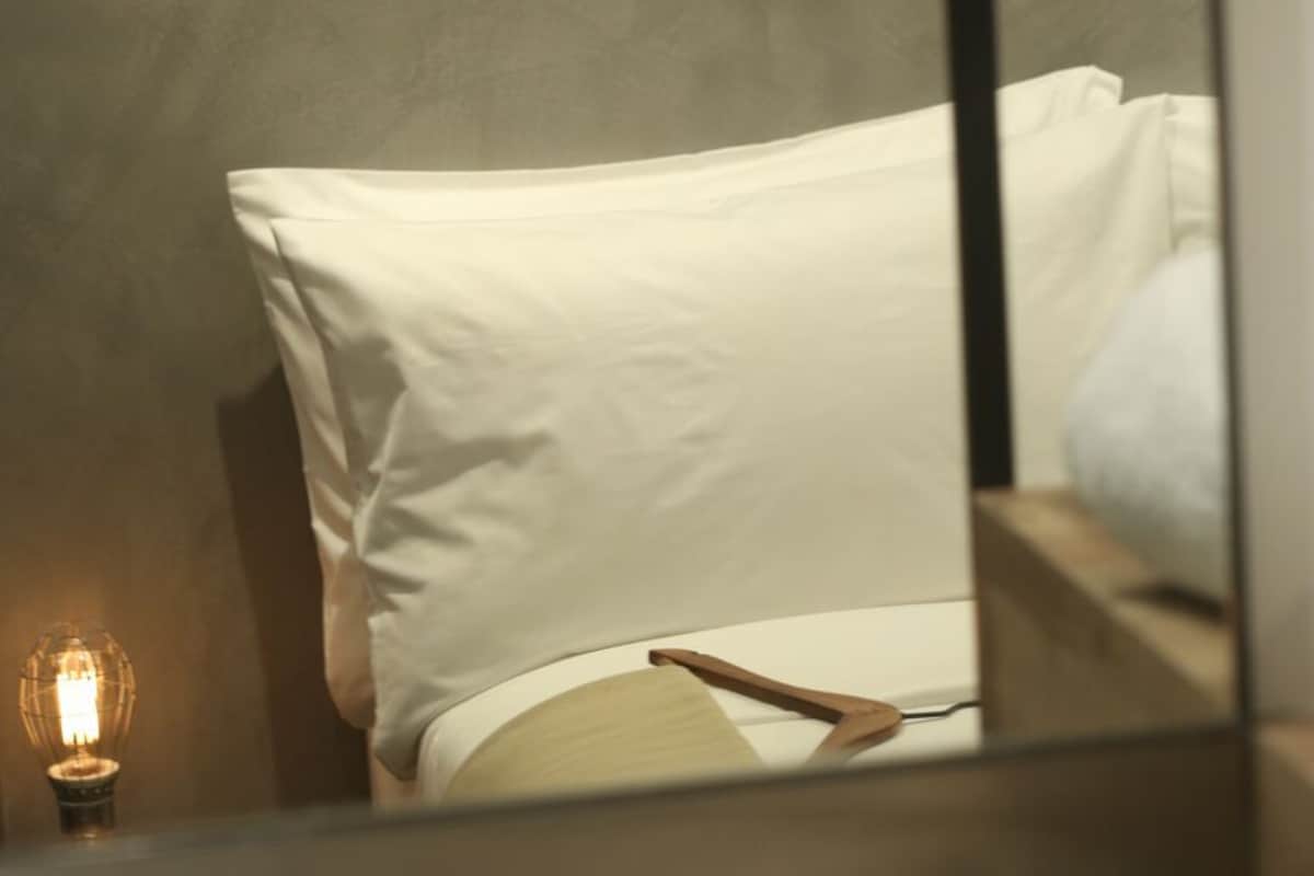Quarto com cama, abajur e espelho refletindo a cama.