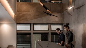 Un interior moderno con una mesa central geométrica, ventanas amplias y lámparas colgantes.