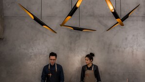 Dos personas detrás de un mostrador, con un techo moderno de estilo industrial e iluminación colgante.