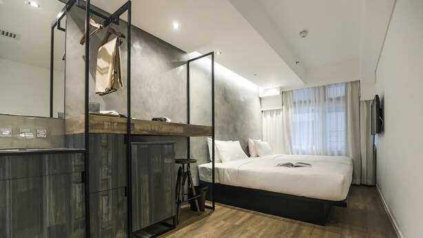 Un dormitorio moderno con una cama grande, un armario de madera, una mesita pequeña y un espejo.
