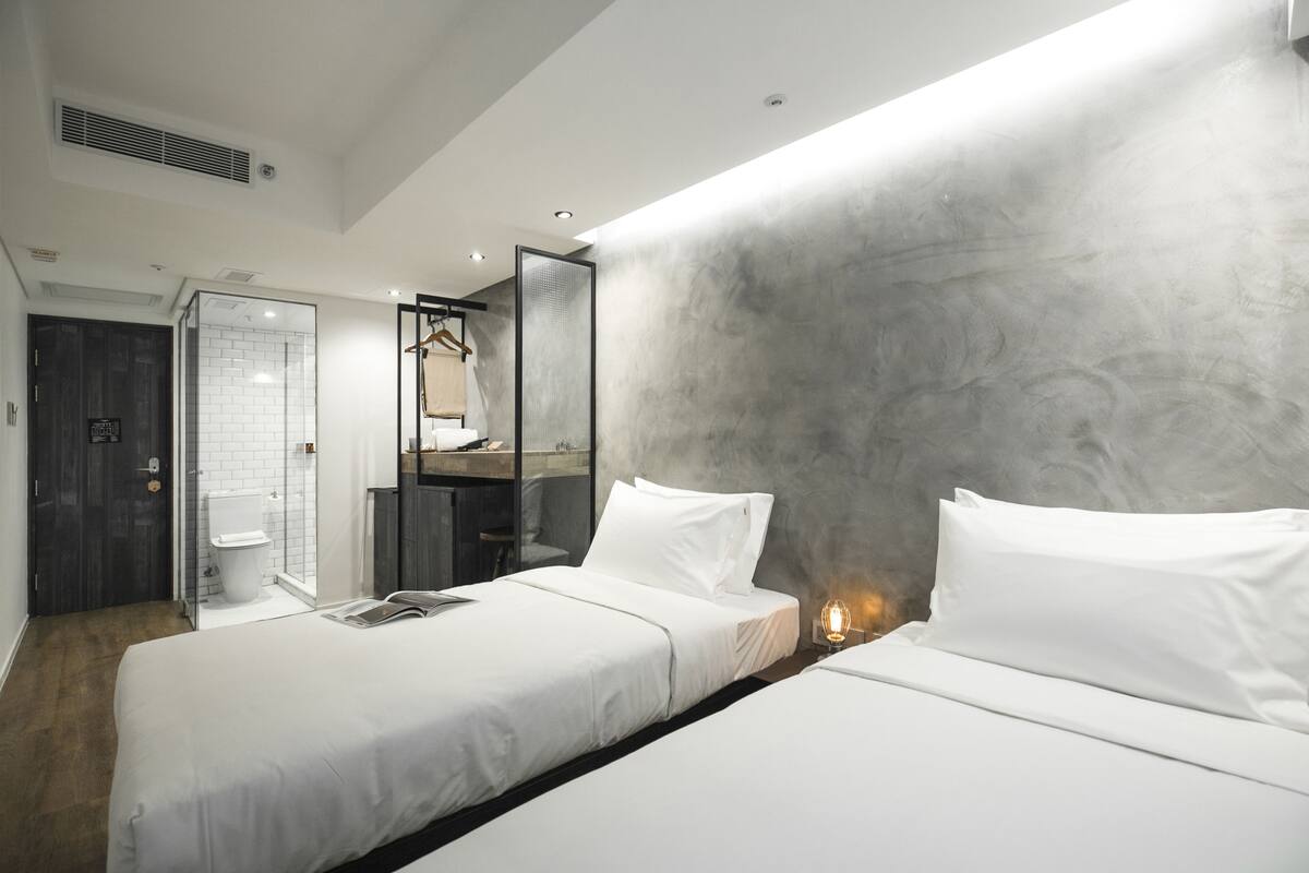 Una habitación de hotel moderna con una cama grande, ducha a ras de suelo y un espejo amplio.