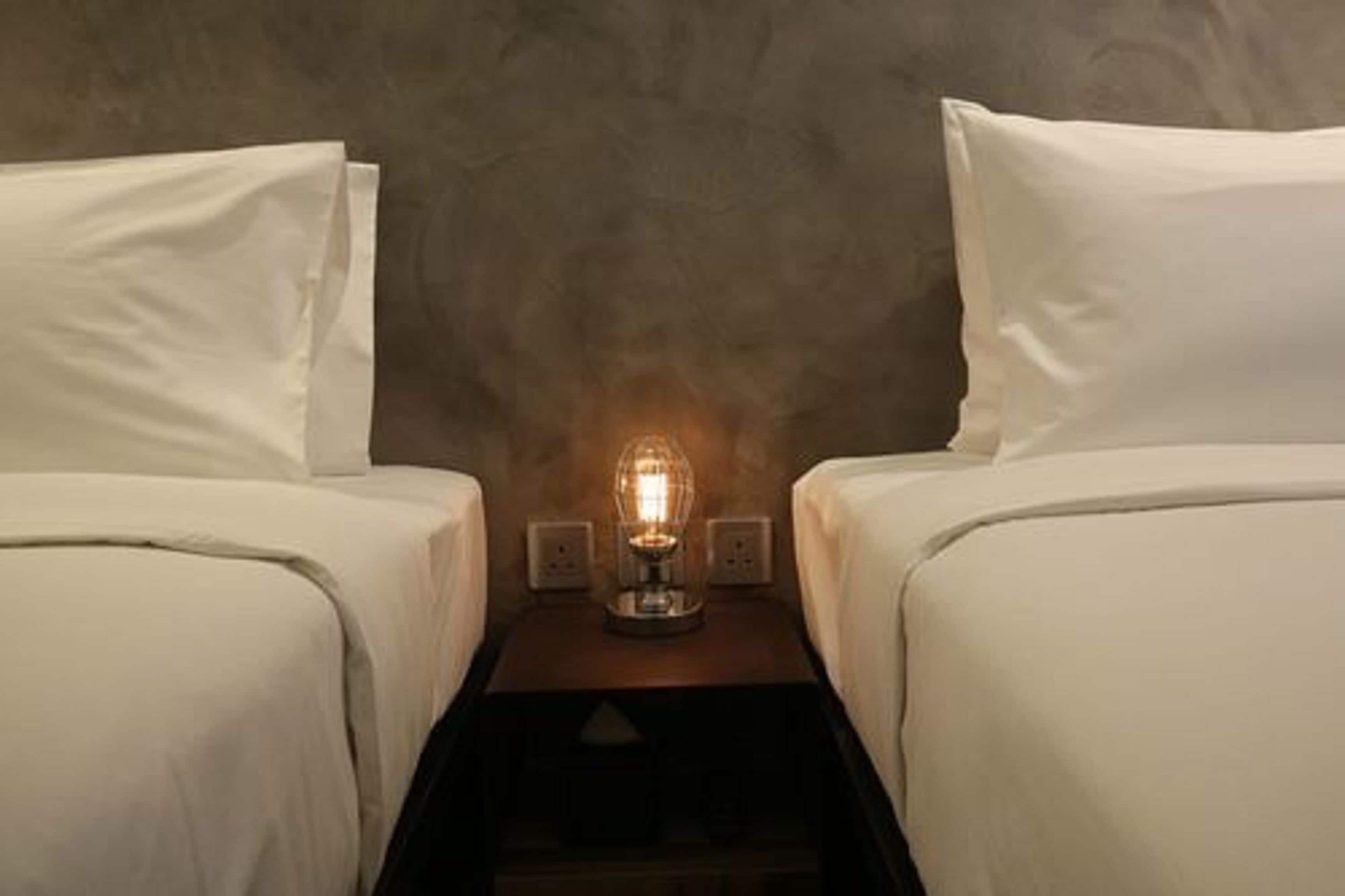 A hotel room with two beds, a nightstand with a lamp, and a textured wall.