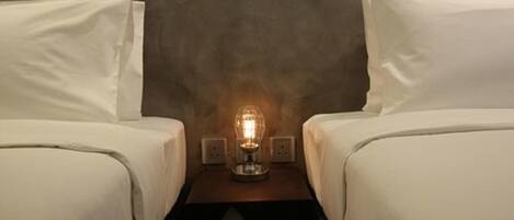 A hotel room with two beds, a nightstand with a lamp, and a textured wall.
