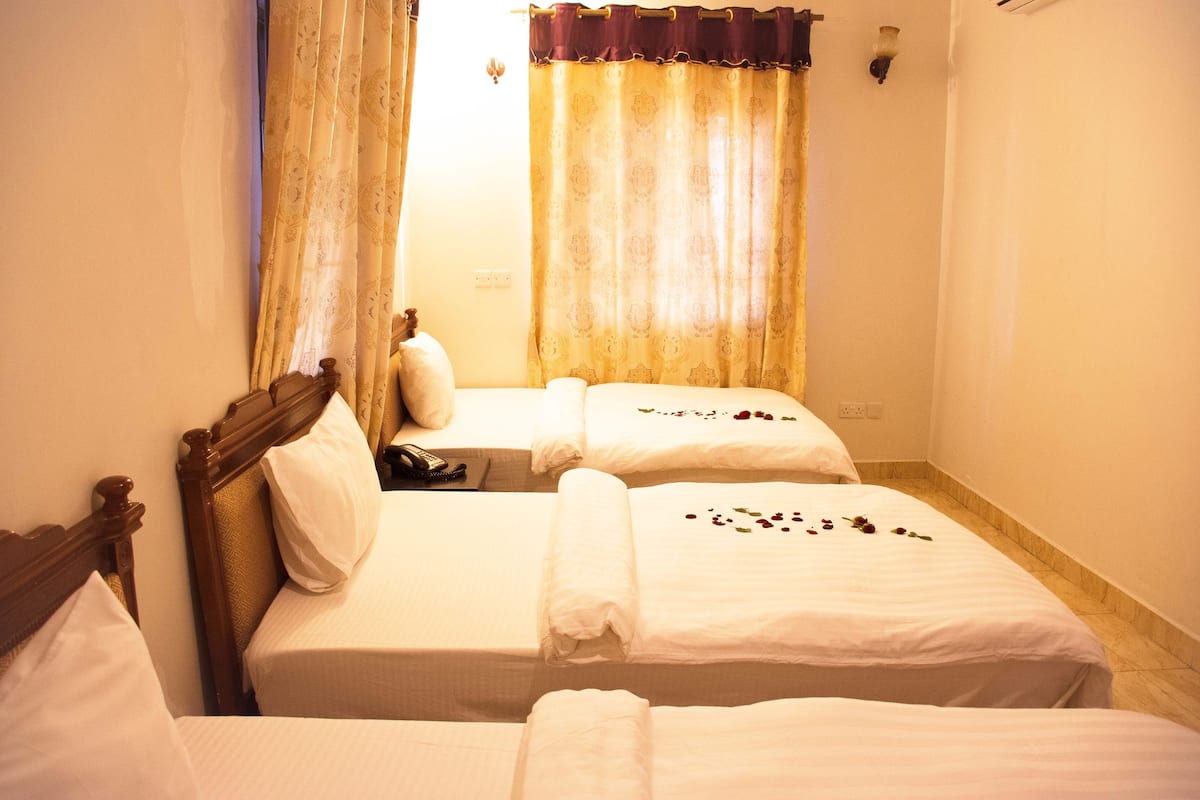 A hotel room with two beds, a wooden headboard, a telephone, and a window with curtains.