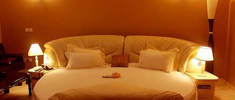 Una cama grande con cabecera, dos lámparas de noche y una mesita con lámpara.