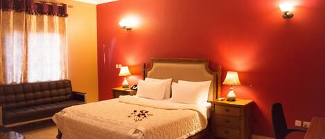 Habitació d'hotel amb un llit gran, dues taules de nit amb làmpades, un taulell de nit de fusta, un sofà de pell negra i un escriptori de fusta.