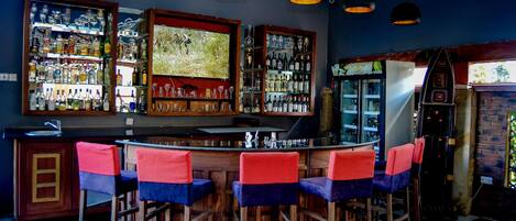 Una zona de bar con suelo de cuadros, barra de madera y varios taburetes.