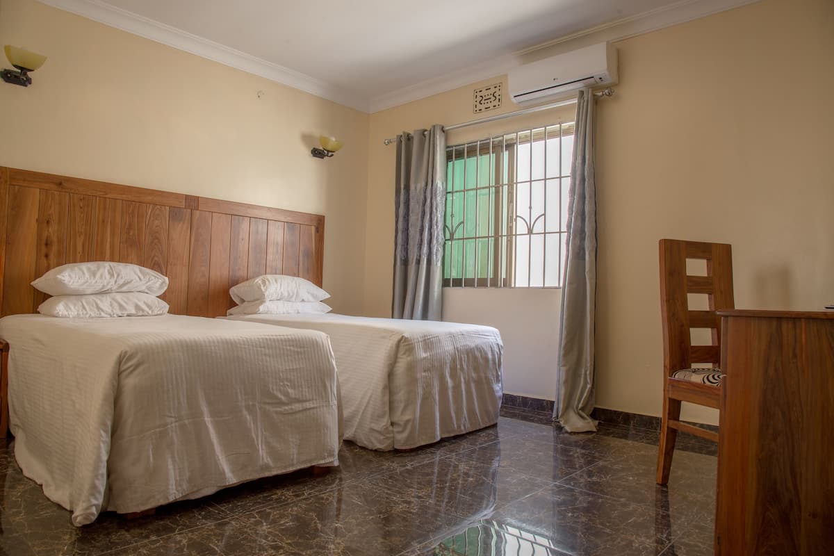 A hotel room with two beds, a wooden headboard, a desk, and a window with curtains.
