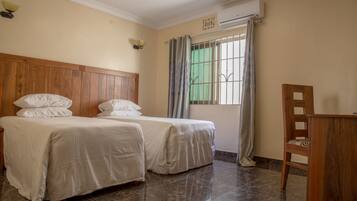A hotel room with two beds, a wooden headboard, a desk, and a window with curtains.