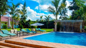 Una piscina con escalones de acceso, rodeada de sillas de descanso y sombrillas.