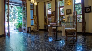 Un vestíbulo con suelo de mármol, una silla de madera, una mesa con un jarrón y un cartel que indica una sala de conferencias.