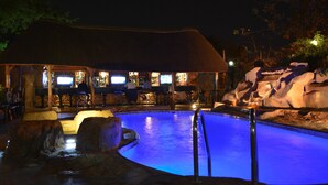 A swimming pool with a thatched-roof structure and a bar area. - Elevate Suites (Kigali)