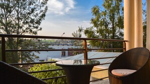 A balcony with wicker chairs and a glass table, overlooking a body of water and greenery. - Elevate Suites (Kigali)