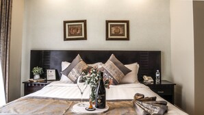 A neatly made bed with pillows, a bottle of wine, and a small vase of flowers on the bedside table. - Elevate Suites (Kigali)