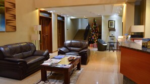 A hotel lobby with leather sofas, a reception desk, a Christmas tree, and a staircase. - Elevate Suites (Kigali)