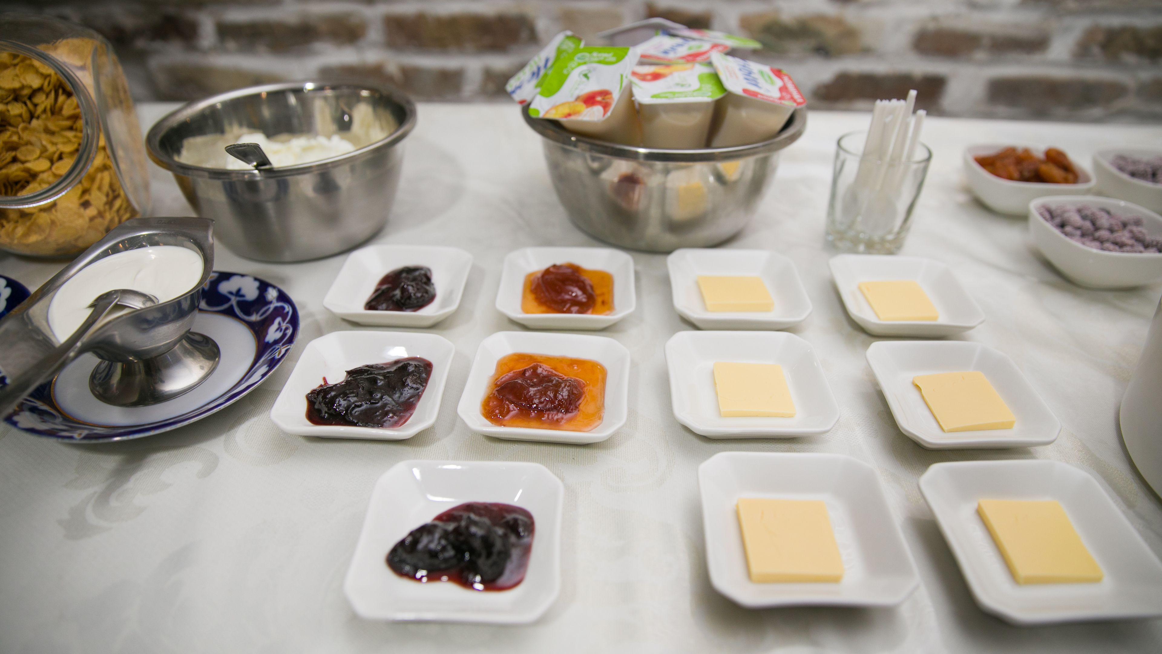 Una mesa con diversos alimentos y condimentos, como tazones de yogur, queso y mermeladas.
