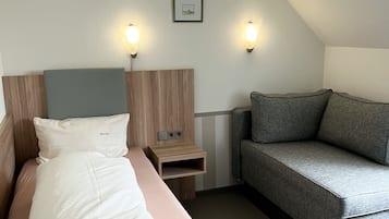 A modern hotel room with a bed, a nightstand, a sofa, and two wall-mounted lights.