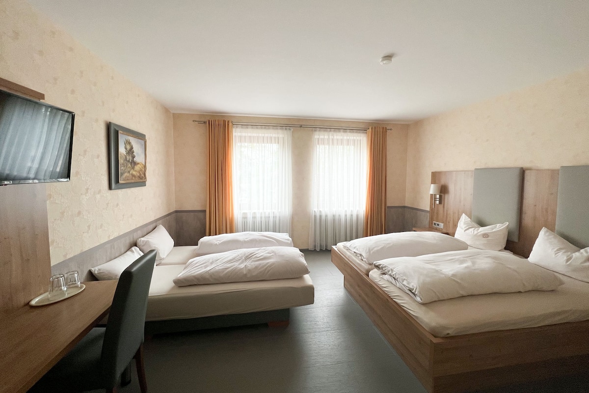 A hotel room with two beds, a desk, a chair, a TV, and a window with curtains.