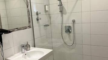 Un baño con lavamanos blanco, un espejo y cabina de ducha con mampara de vidrio.