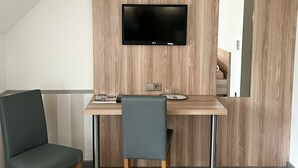 A modern room with a flat-screen TV mounted on a wooden wall, a dining table with chairs, and a large mirror. - Hotel Garni Illertal (Altenstadt)