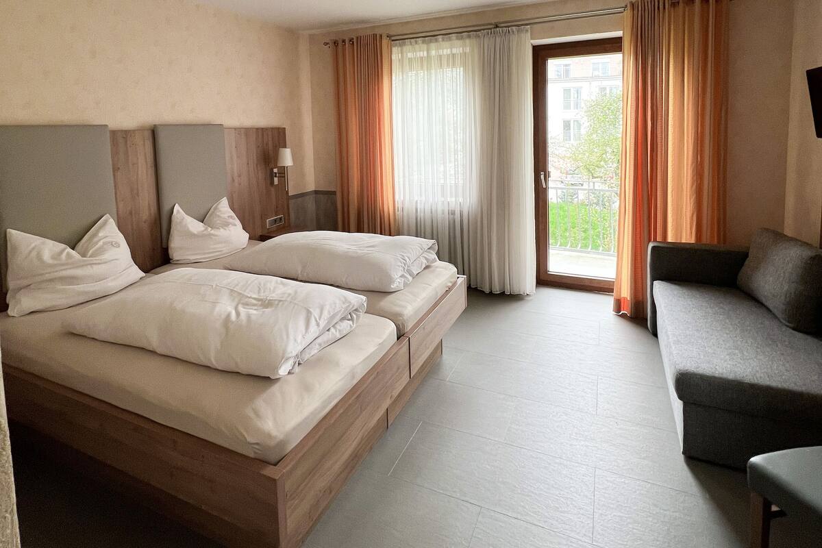 A hotel room with two beds, a sofa, and a large window with curtains.