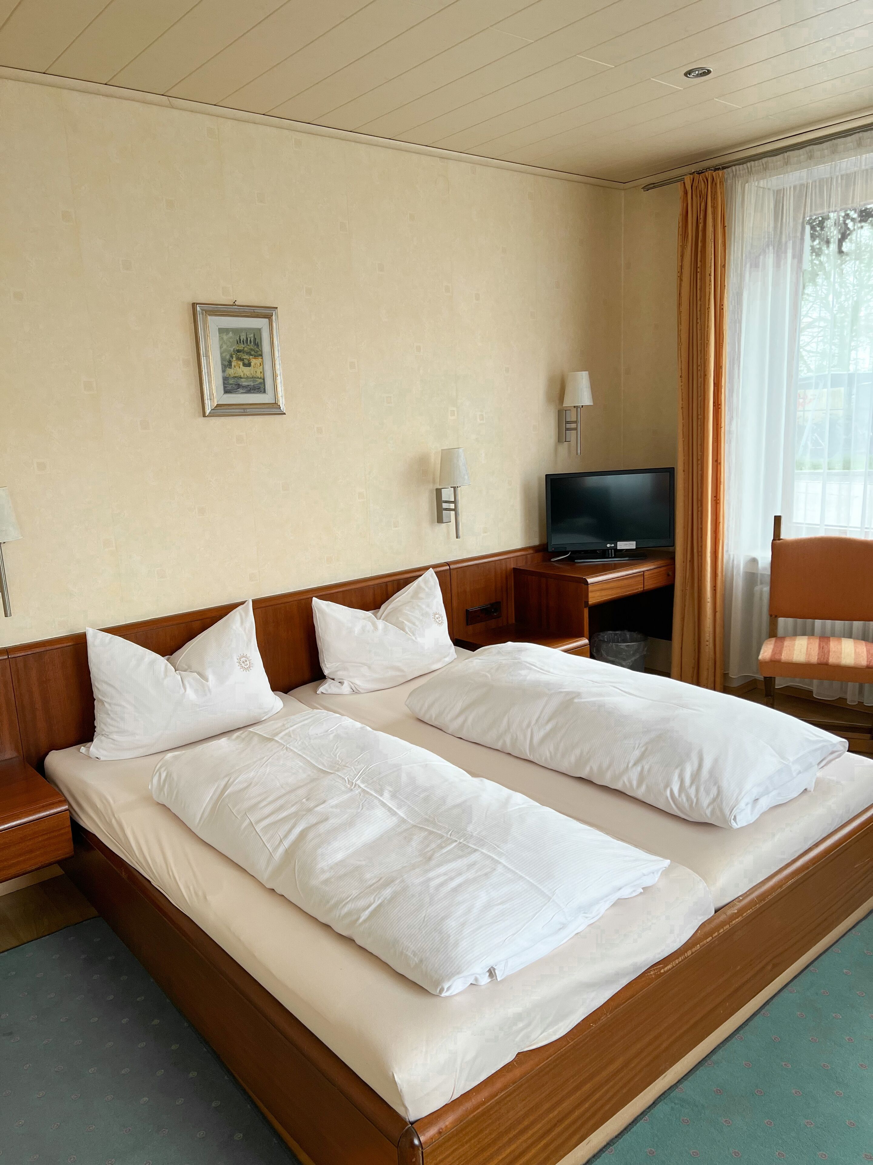 A hotel room with two single beds, a television, a desk, and a chair.