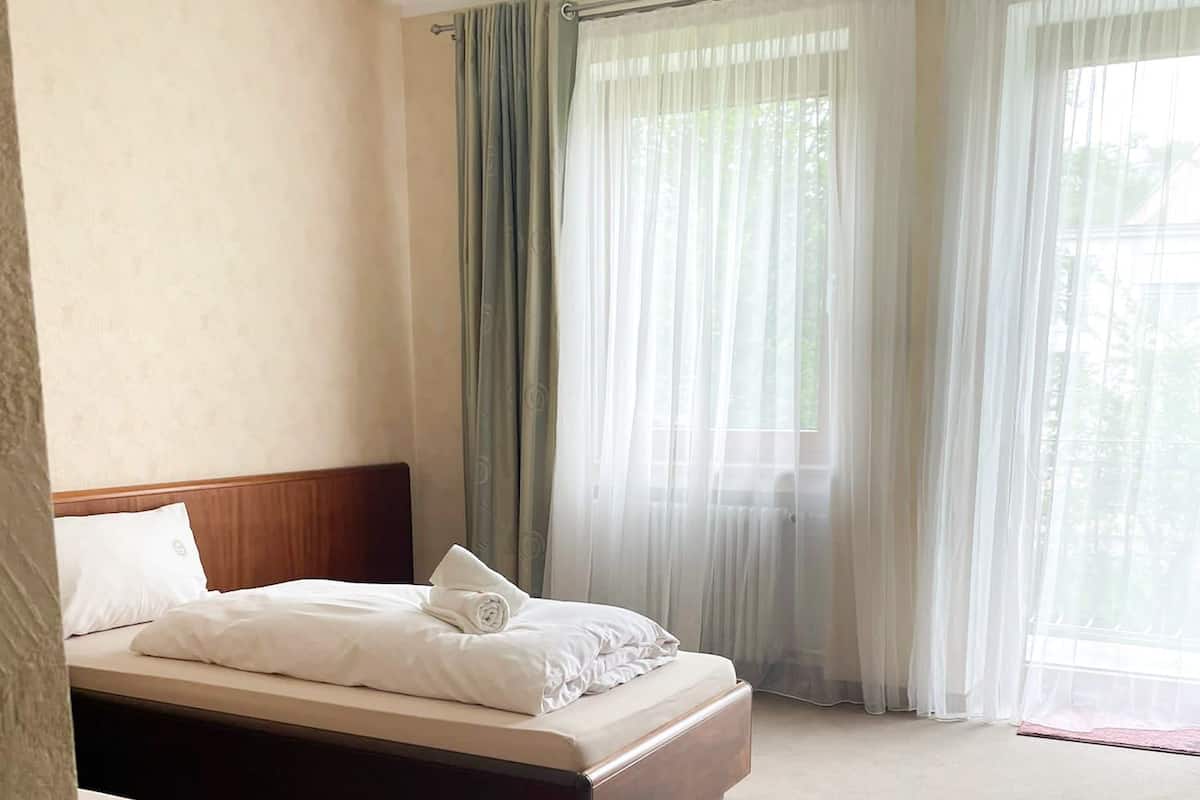A hotel room with a large bed, a smaller bed, and a window with sheer curtains.