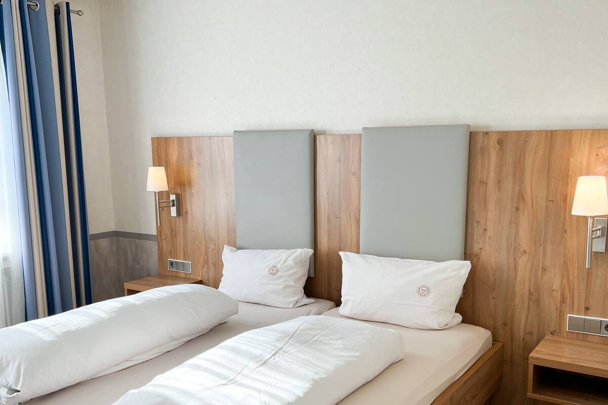 A double bed with a wooden frame and headboard, two bedside tables with lamps, and a window with curtains.