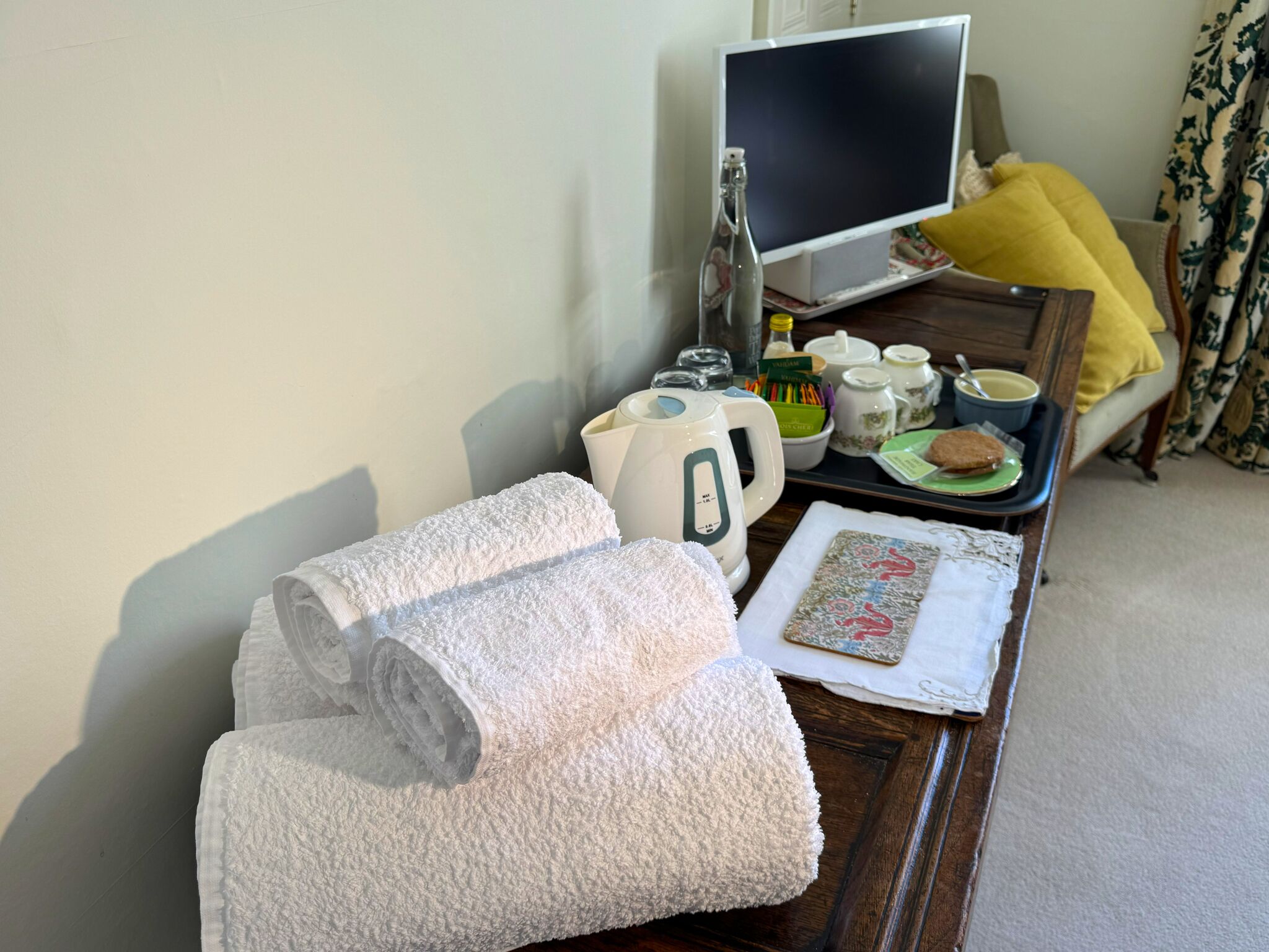 Habitación de hotel impecable con una cama, una mesita de noche con una tetera, tazas y una bandeja con alimentos.