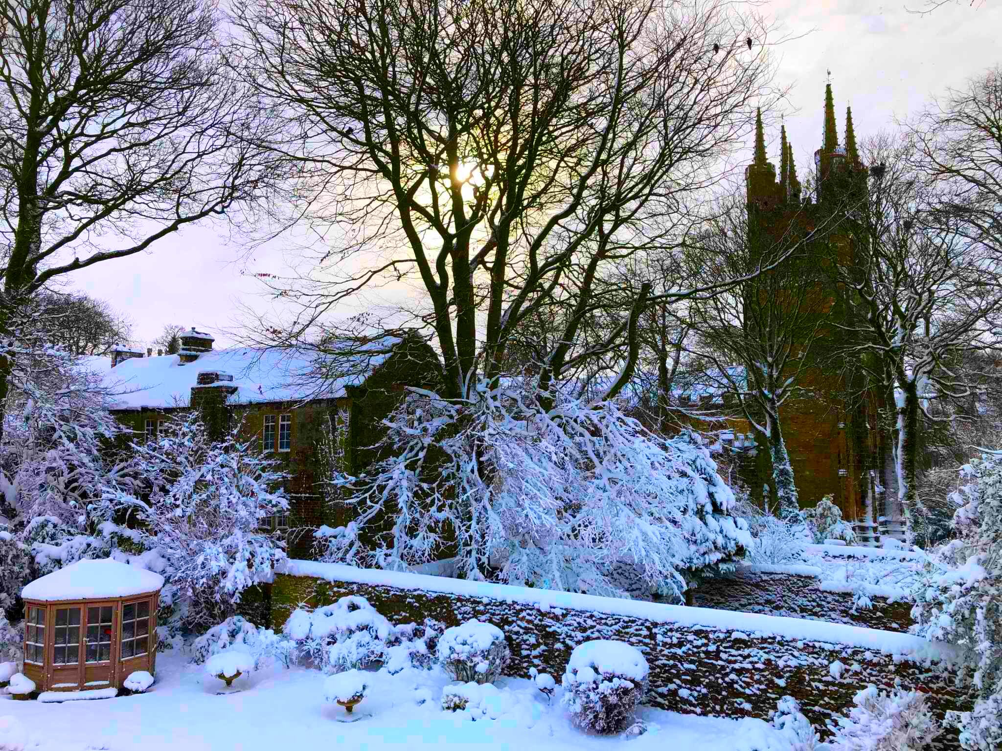 A snow-covered landscape with a historic building, a stone bridge, and a church tower.
