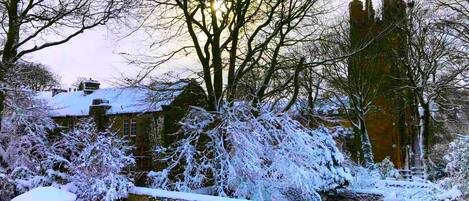 A snow-covered landscape with a historic building, a stone bridge, and a church tower.