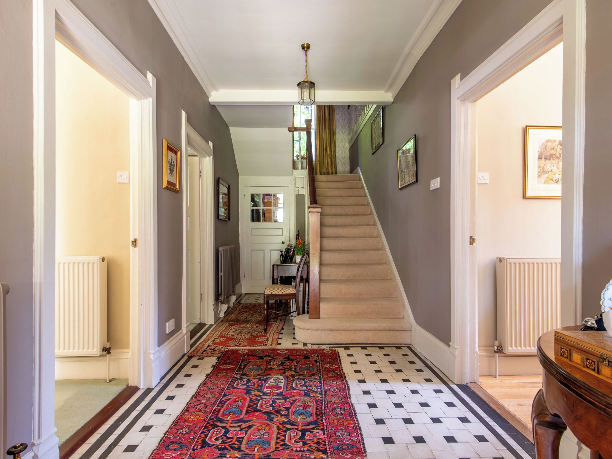 Un pasillo con alfombra estampada, una escalera y un radiador.
