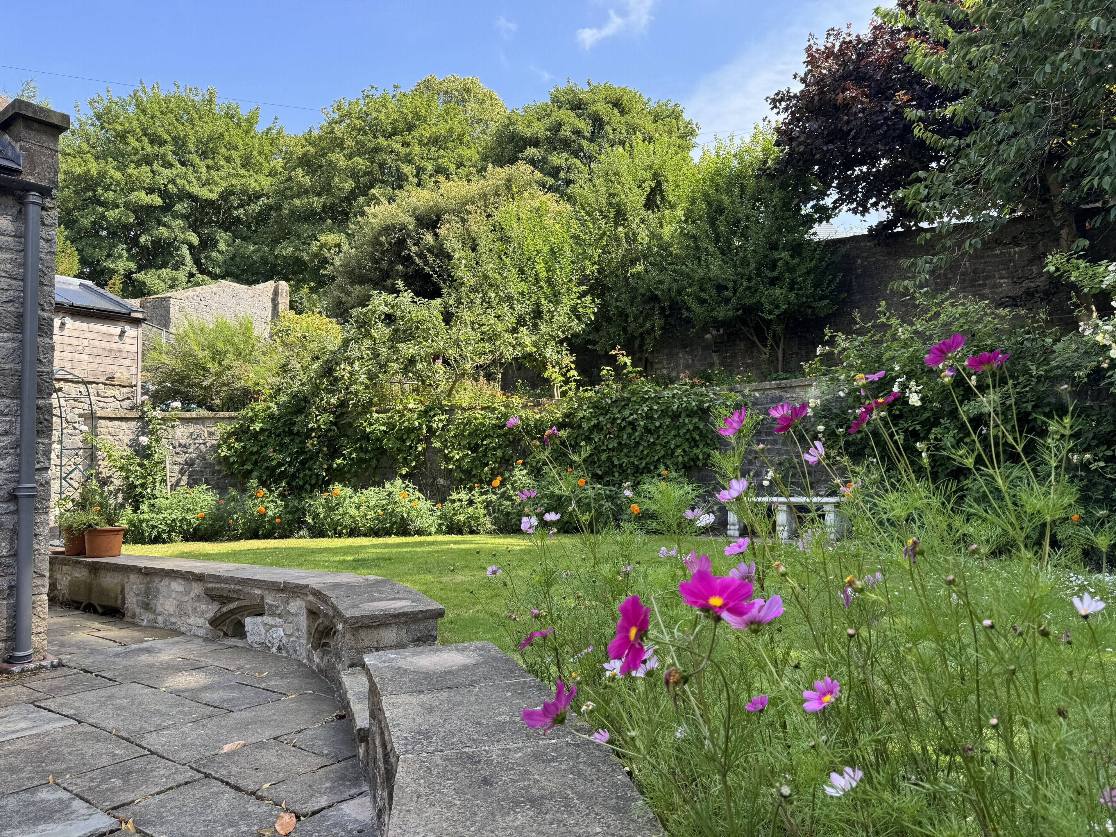 A garden with a stone bench, a stone wall, and a variety of flowers.