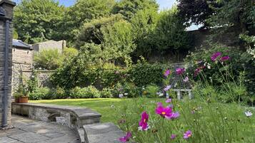 A garden with a stone bench, a stone wall, and a variety of flowers.