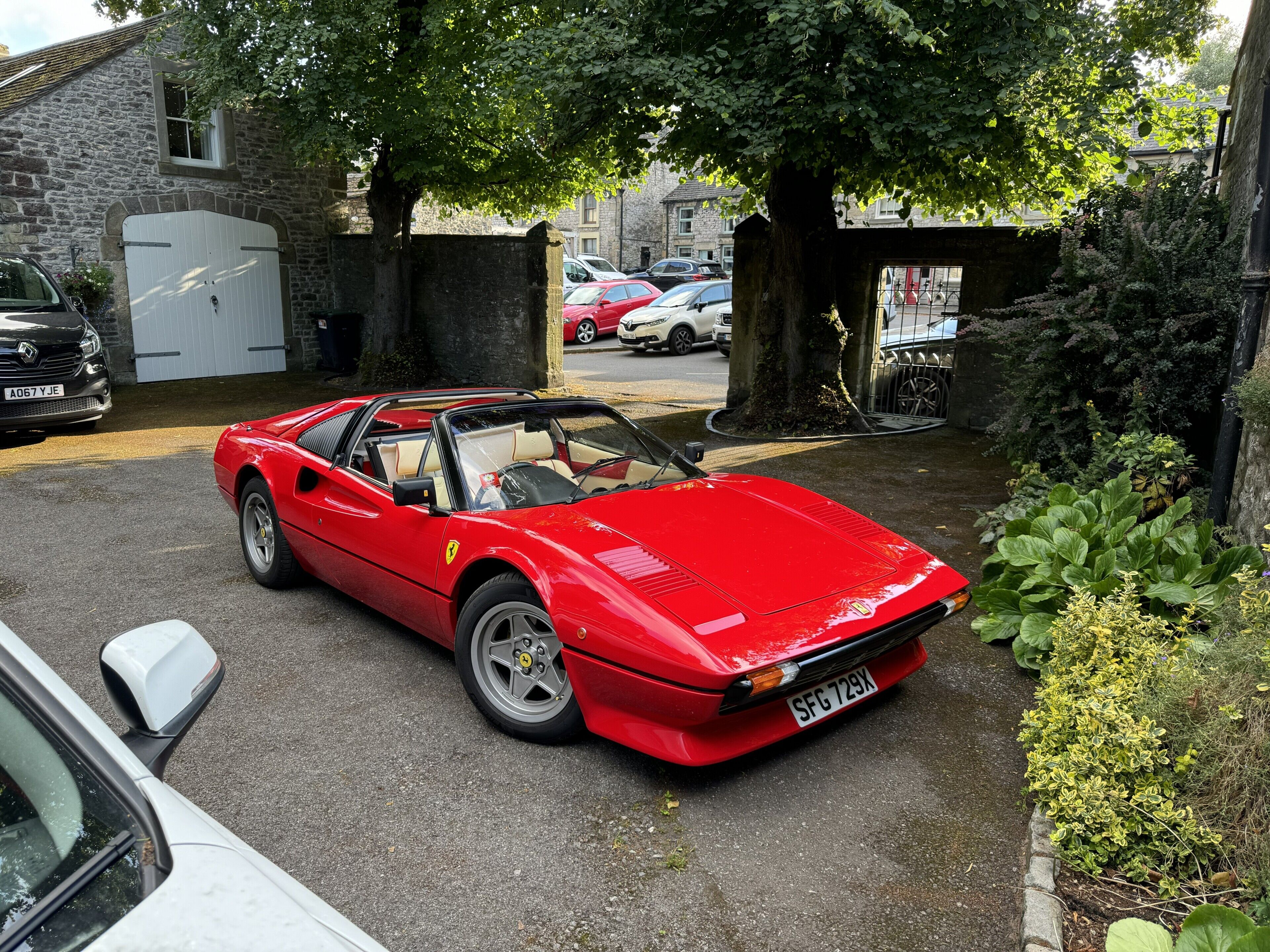 A red sports car parked in a driveway with a stone wall and greenery in the background.