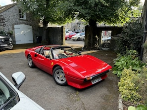 A red sports car parked in a driveway with a stone wall and greenery in the background. - The Old Vicarage B&B (Buxton)