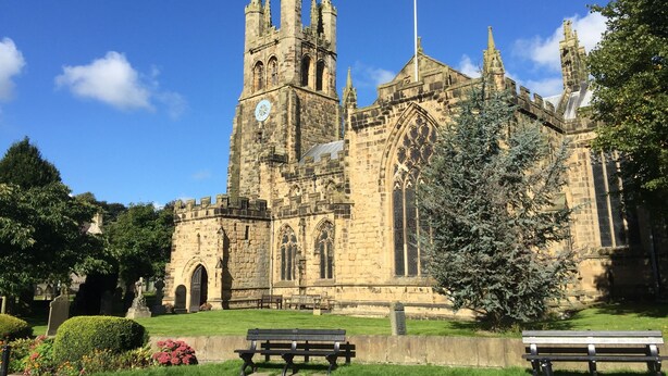 A historic church with a tall tower and Gothic architecture, surrounded by a well-maintained lawn and benches. - The Old Vicarage B&B (Buxton)